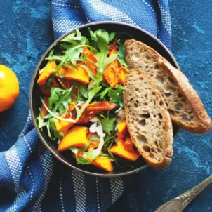 Vegan skillet meal with bread, spices, orange, and utensils on blue table