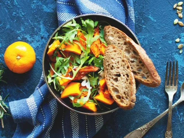 Vegan skillet meal with bread, spices, orange, and utensils on blue table