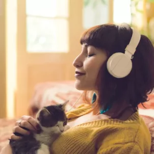 Woman on floor in bedroom holding kitten listening to meditation app on headphones