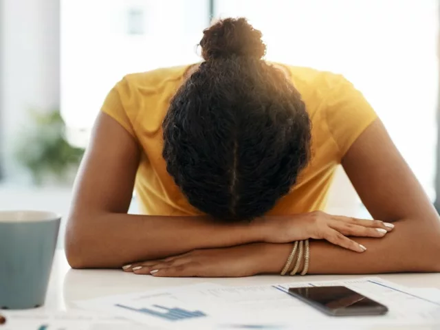 Dark-haired woman exhausted from work burnout resting her head at her desk