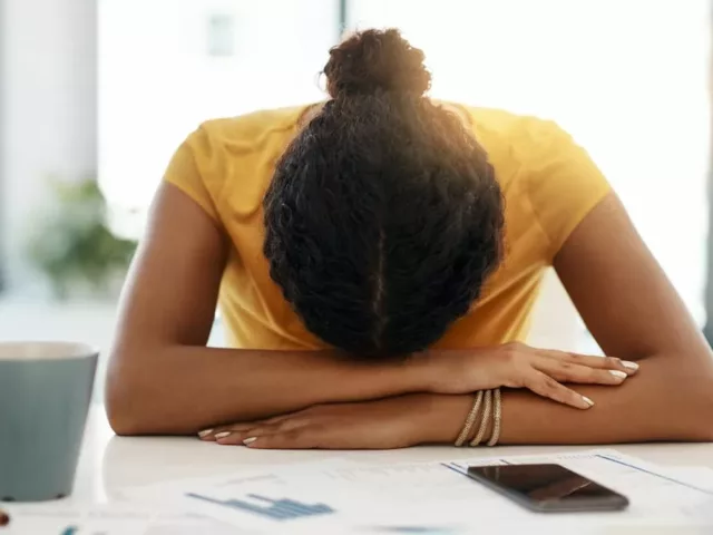 Dark-haired woman exhausted from work burnout resting her head at her desk