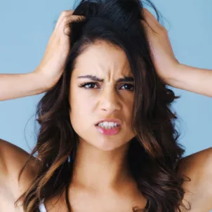 Woman holding head in her hands stressed about hair loss on blue background