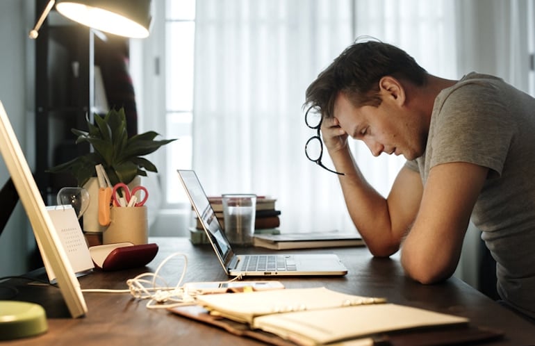 Stressed man suffering from symptoms of burnout at home in front of laptop