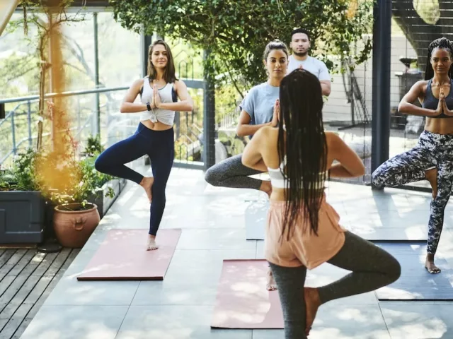 Small group yoga class performing tree pose on outdoor patio