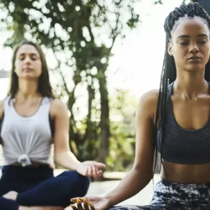 Two women doing seated meditation at a yoga class outdoors