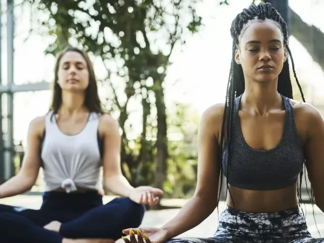 Two women doing seated meditation at a yoga class outdoors