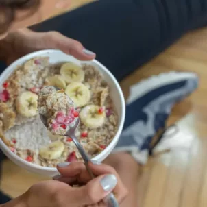 Woman in athletic clothes eating a bowl of oats, berries, and pomegranate