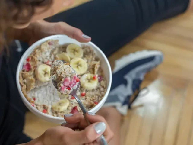 Woman in athletic clothes eating a bowl of oats, berries, and pomegranate