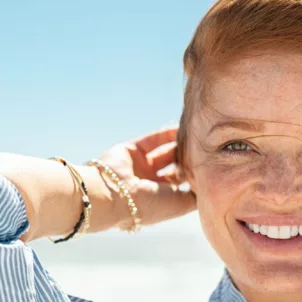 Red-haired woman with clear skin and freckles smiling at beach in summer