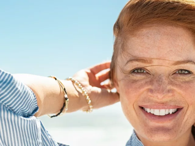 Red-haired woman with clear skin and freckles smiling at beach in summer