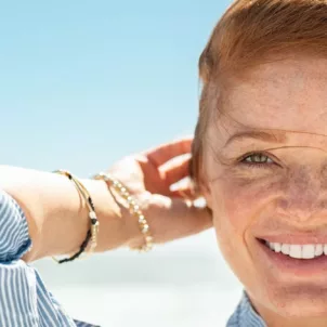 Red-haired woman with clear skin and freckles smiling at beach in summer