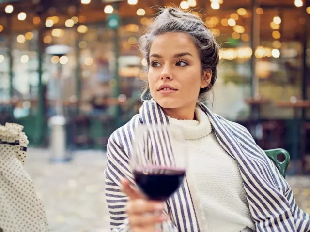 Woman sitting at chic restaurant outdoors with a glass of red wine