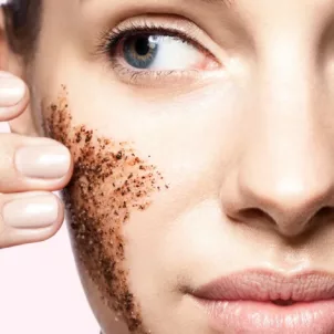 Close up of woman using dark physical exfoliant on pink background