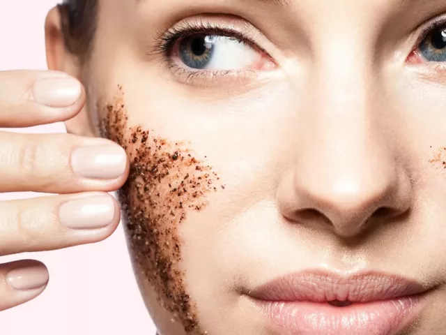 Close up of woman using dark physical exfoliant on pink background