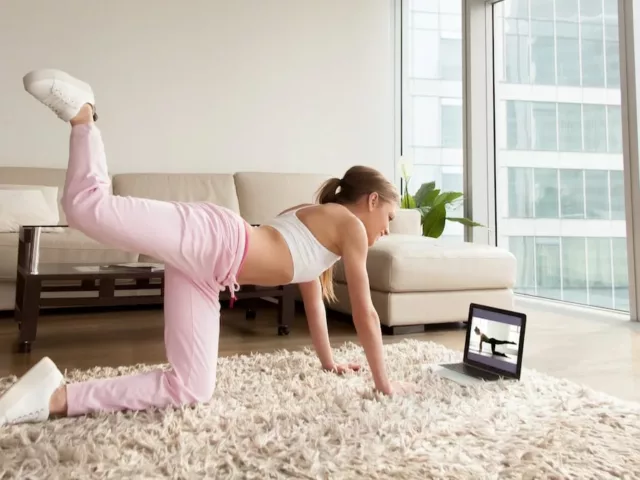 Woman in athletic gear working out in her living room with an online fitness program