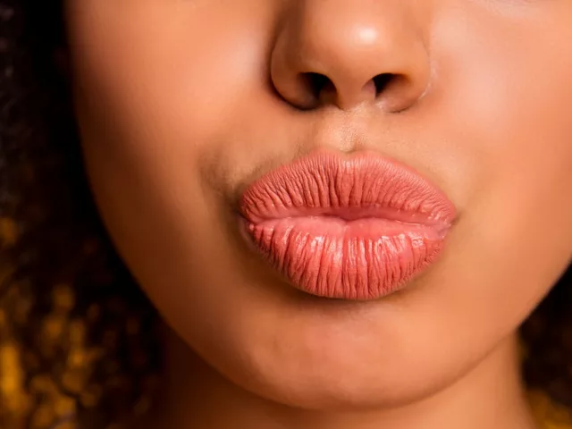 Woman puckering her coral lips in front of orange background