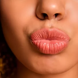 Woman puckering her coral lips in front of orange background