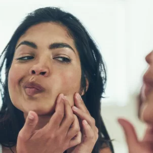 Woman looking in mirror for blackheads and breakouts