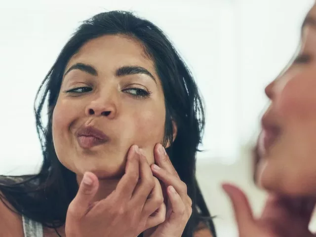 Woman looking in mirror for blackheads and breakouts