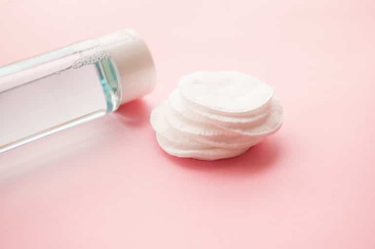 Facial toner and cotton pads on baby pink background