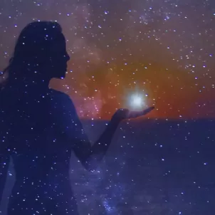 Woman holding a shining star in her hand in the colorful dreamy night sky