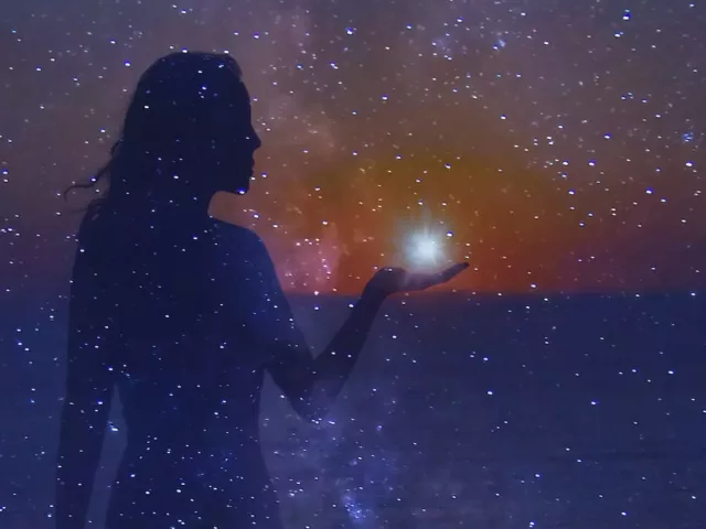 Woman holding a shining star in her hand in the colorful dreamy night sky