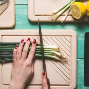 Overhead shot of woman cutting scallions with tablet for recipes by her side