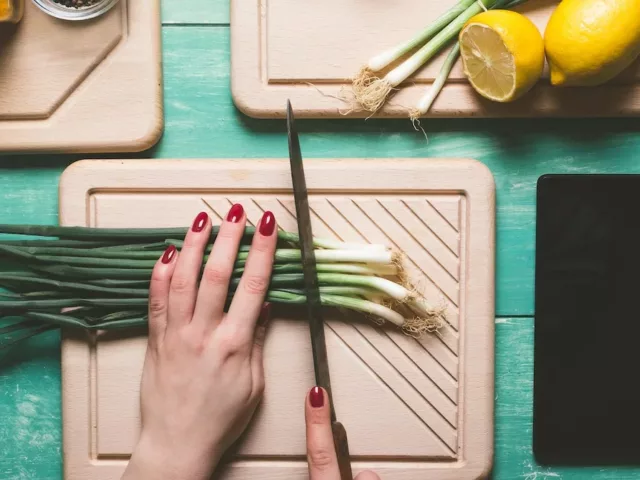 Overhead shot of woman cutting scallions with tablet for recipes by her side