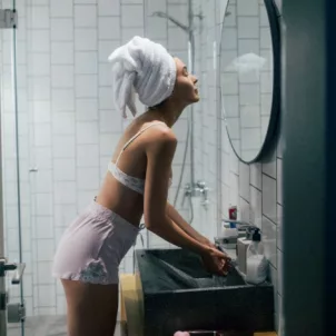 Young woman with towel around head in bathroom performing her nightly skin routine