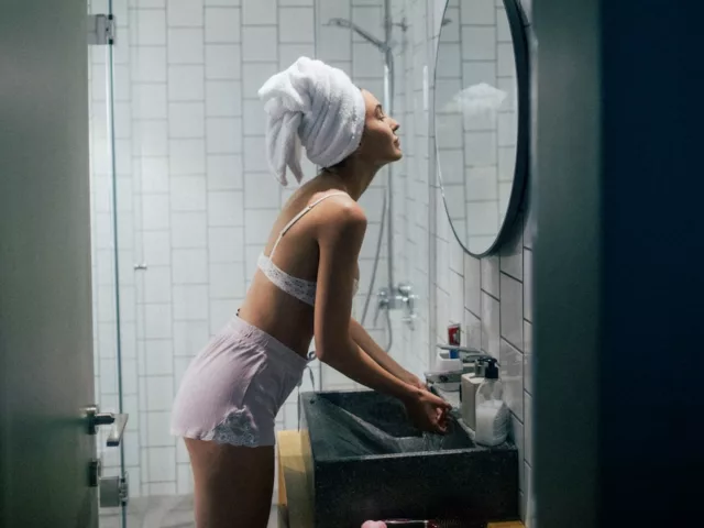 Young woman with towel around head in bathroom performing her nightly skin routine