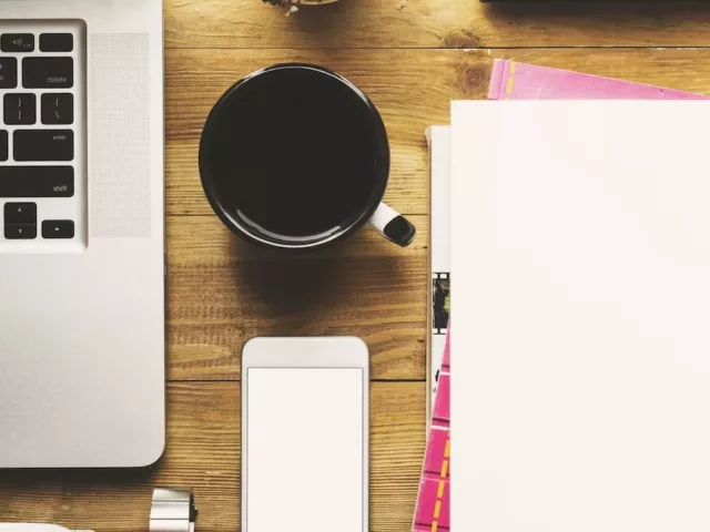 Desk with laptop, coffee, phone, and notebooks organized for optimal productivity