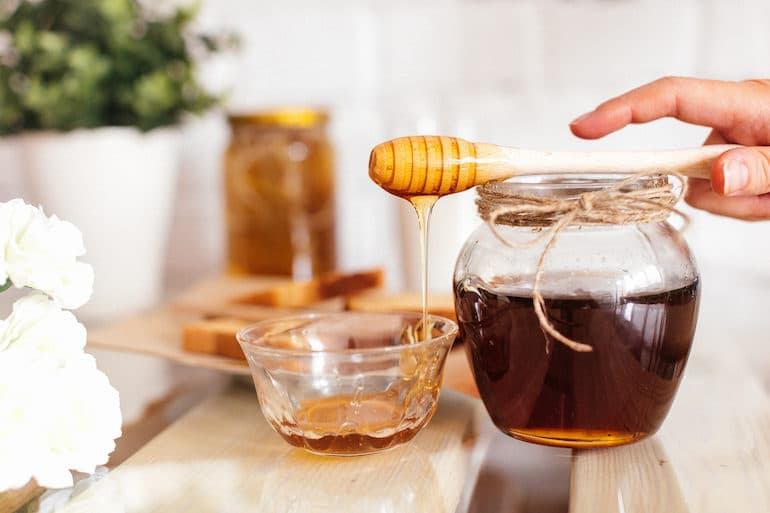 Woman spooling jar of honey with honeycomb