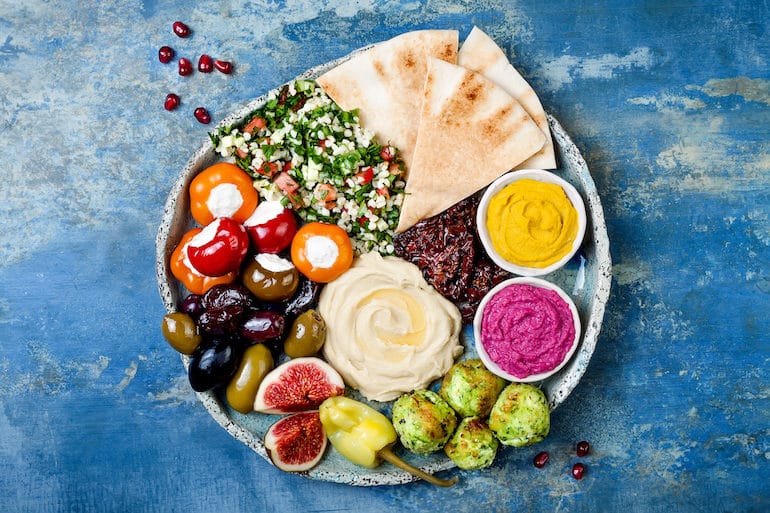 Mediterranean Diet Middle Eastern meze platter with green falafel, pita, sun dried tomatoes, pumpkin and beet hummus, olives, stuffed peppers, tabbouleh, figs. Mediterranean appetizer party idea (Middle Eastern meze platter with green falafel, pita, sun dried tomatoes