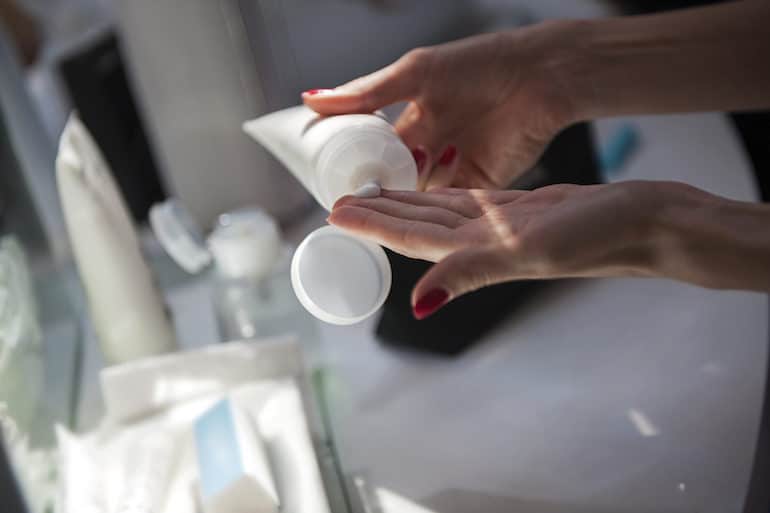 Woman squeezing moisturizer from tube in bathroom