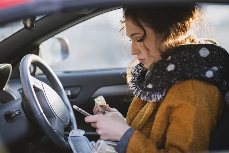 Woman with bad habit of eating in the car while looking at her phone