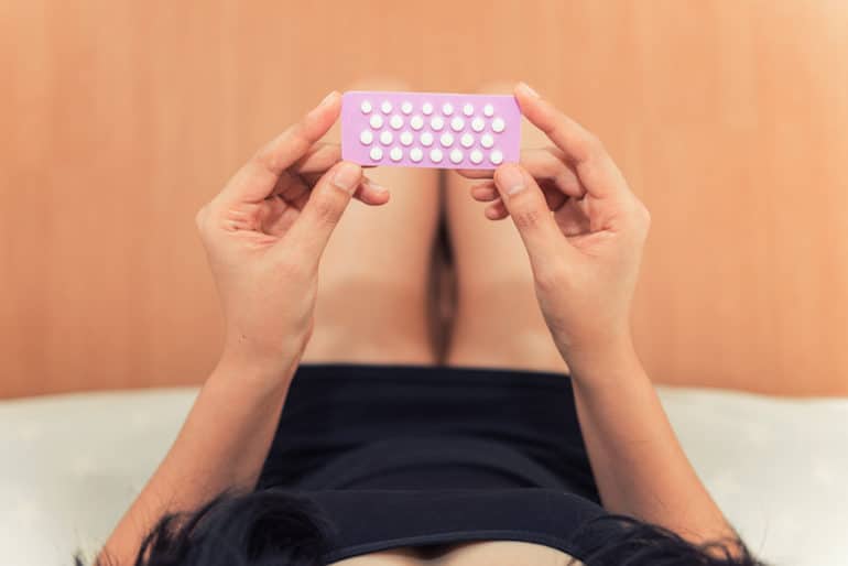 Woman in bed holding purple back of birth control pills