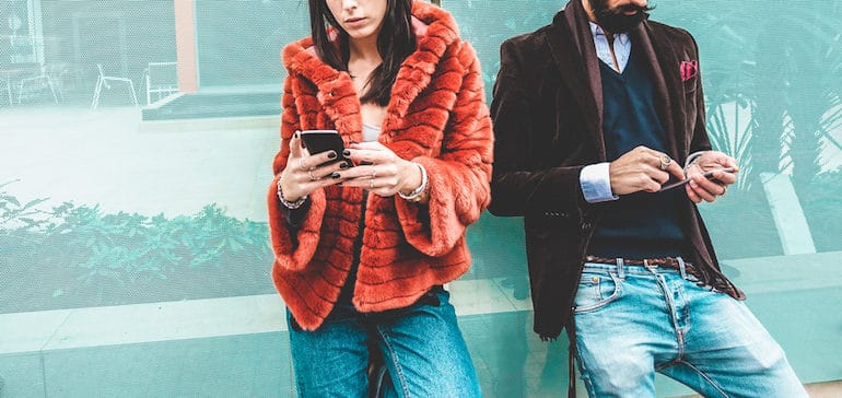 Trendy man and woman on street using social media on smartphones