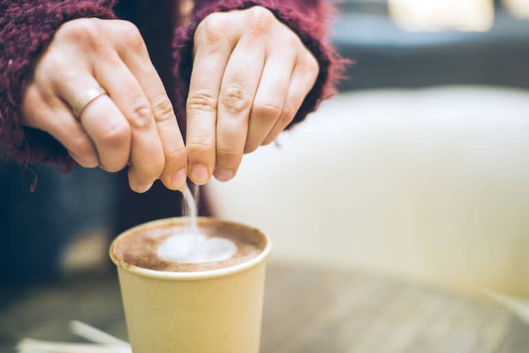 Woman pouring aspartame in coffee