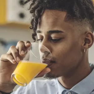 Young man sipping fortified orange juice, which is on the list of vitamin D foods