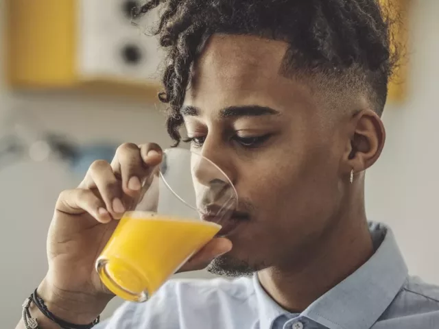 Young man sipping fortified orange juice, which is on the list of vitamin D foods