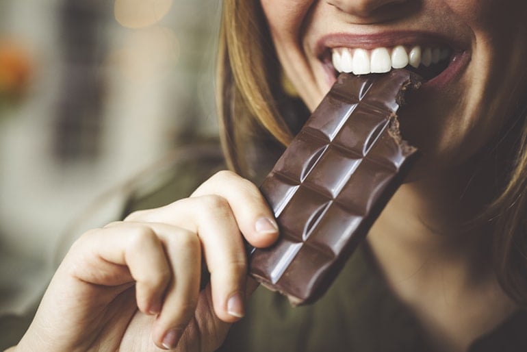 Woman biting into sugary chocolate bar, which may cause breakouts