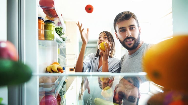 Young couple detoxing their kitchen in front of fridge with fruits and vegetables