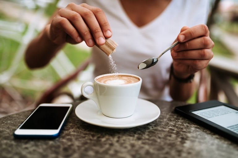 Woman pouring sugar into her morning coffee, which could lead to breakouts