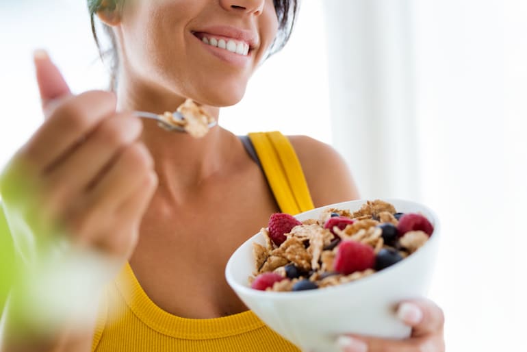 Young woman eating fortified cereal, a good food source of vitamin D, with berries