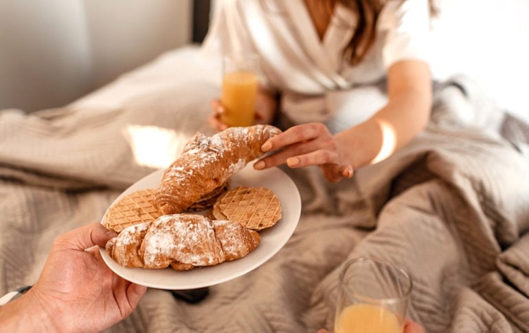 Couple eating croissants in bed to demonstrate link between gluten anc acne