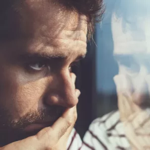 Sad young man looking through the window, discouraged by his own negative self-talk