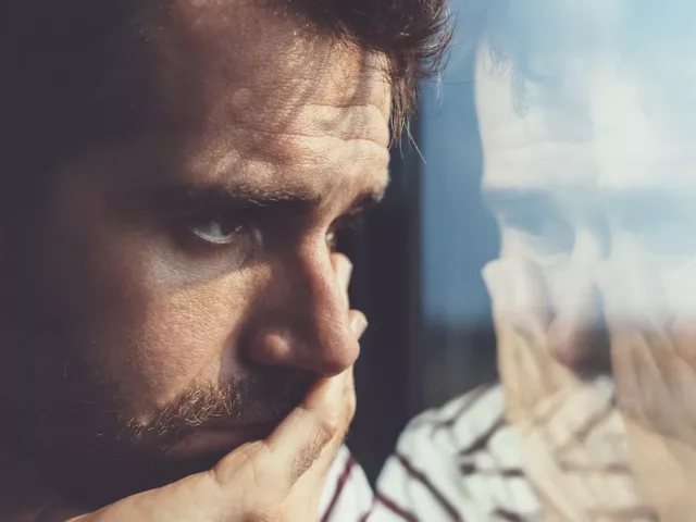 Sad young man looking through the window, discouraged by his own negative self-talk