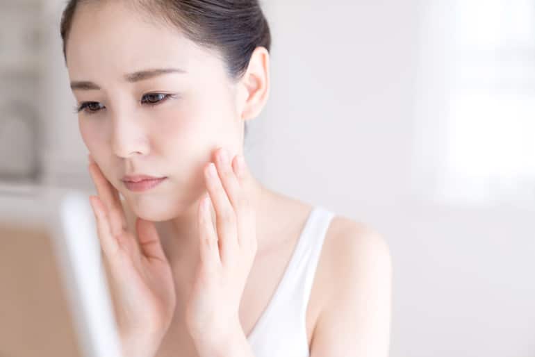 Woman looking sad touching her skin and looking at her face in the mirror