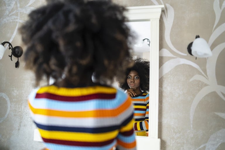 Rear view of woman looking into mirror, discouraged by her negative self-talk