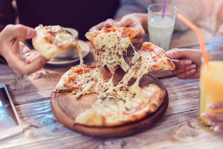 Friends around table grabbing a slice of pizza to satisfy their food cravings for carbs and sugar